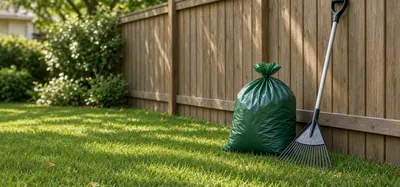 Illustrative photo: a cleaned backyard corner by a wooden fence with one tied waste bag and a rake